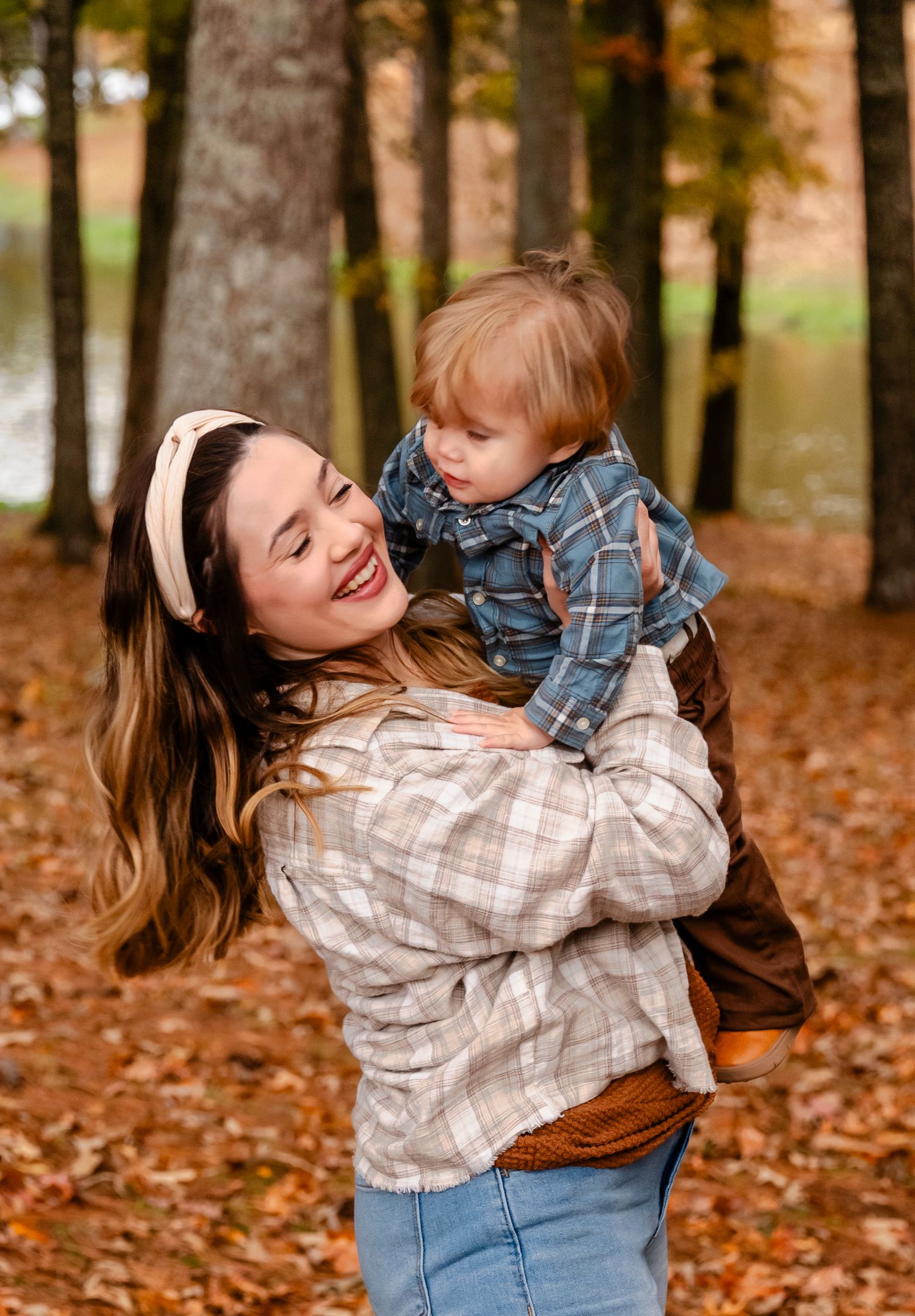 Smiling mother holding toddler in autumn park with colorful fall foliage.