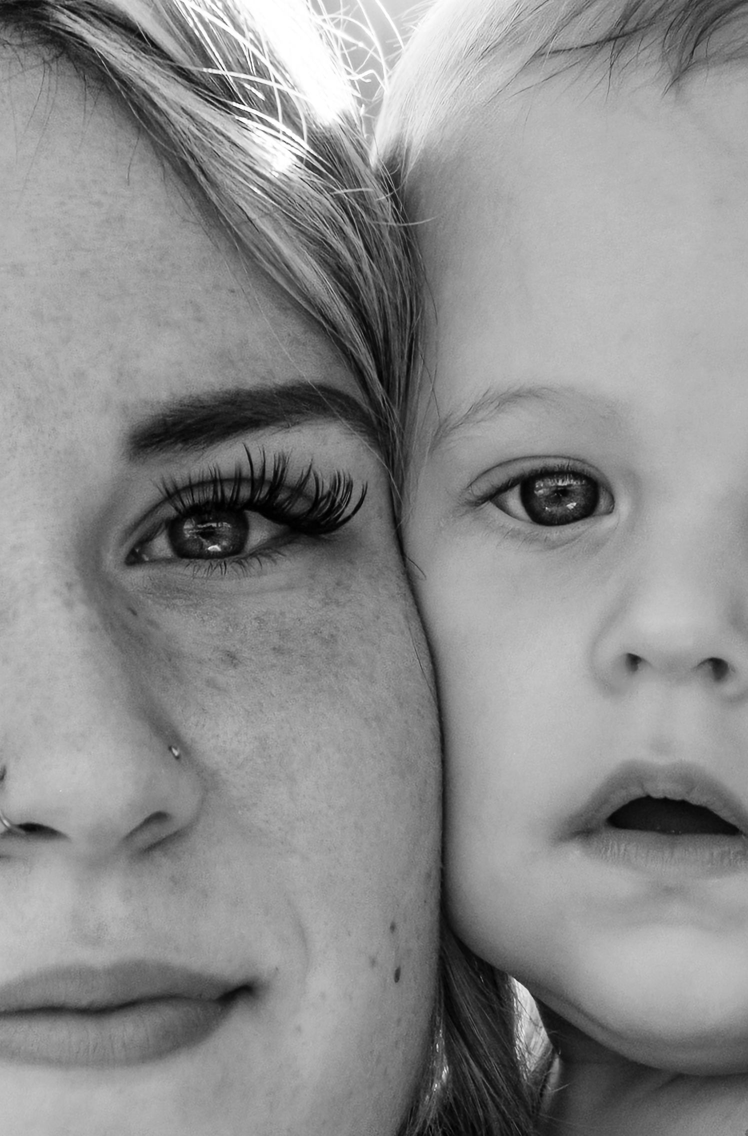 Black and white close-up portrait of a mother and young child cheek to cheek, showing striking eyes and features.