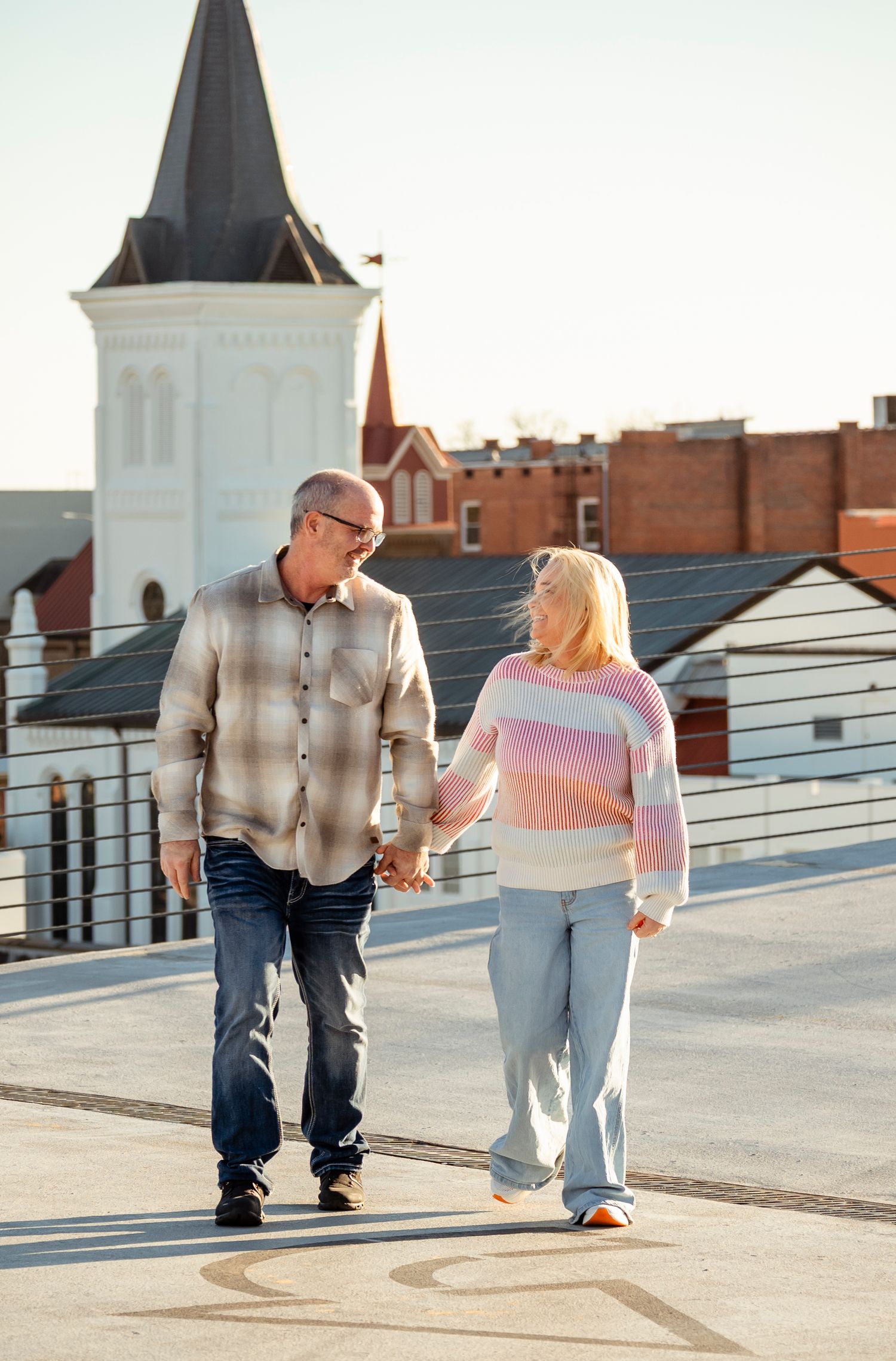 Happy mature couple holding hands and walking on a rooftop with a church steeple behind them.