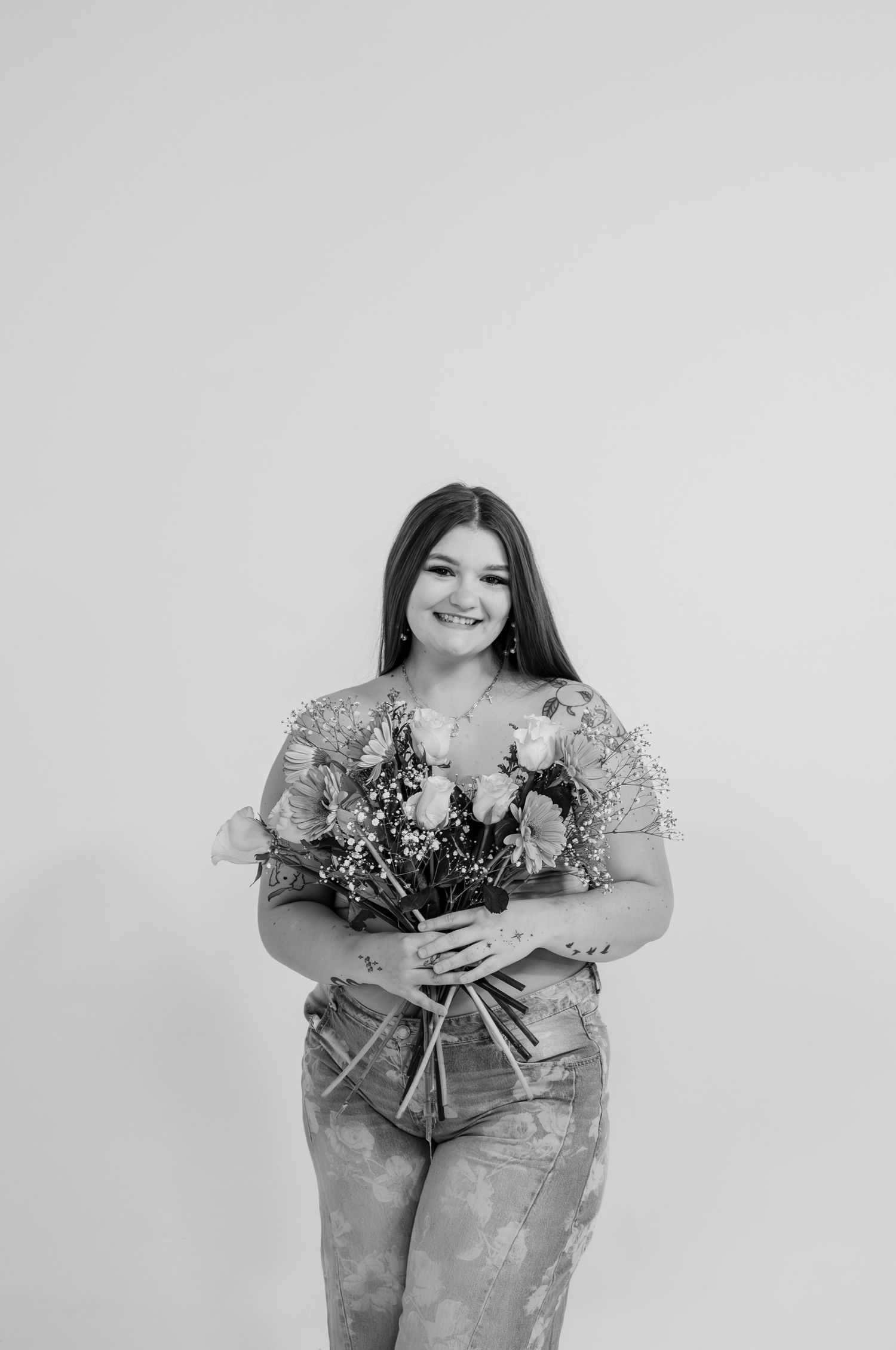 Smiling young woman holds a bouquet of roses and wildflowers in a black and white studio portrait.