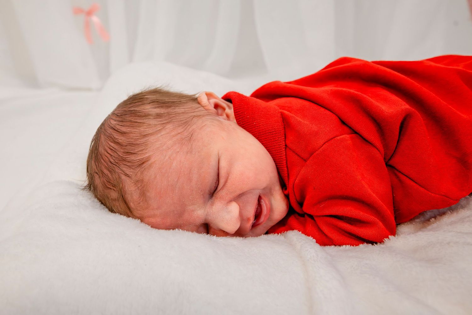 Sleeping newborn baby wrapped in a red outfit lying on a soft white blanket.