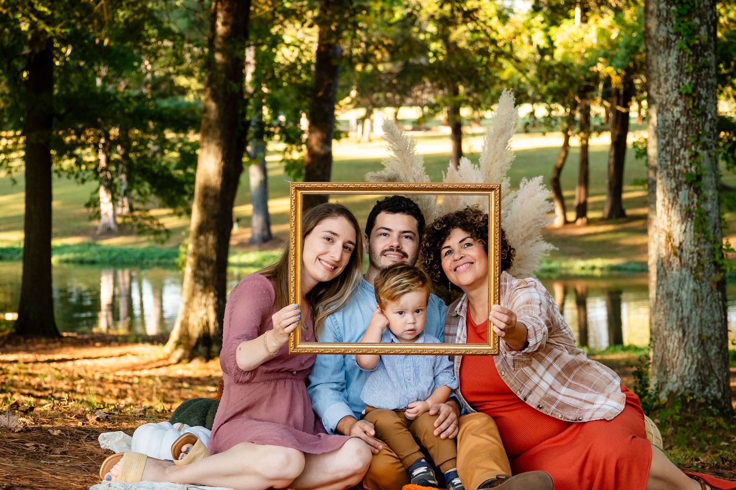 Family of four smiling through decorative gold picture frame in autumn park.
