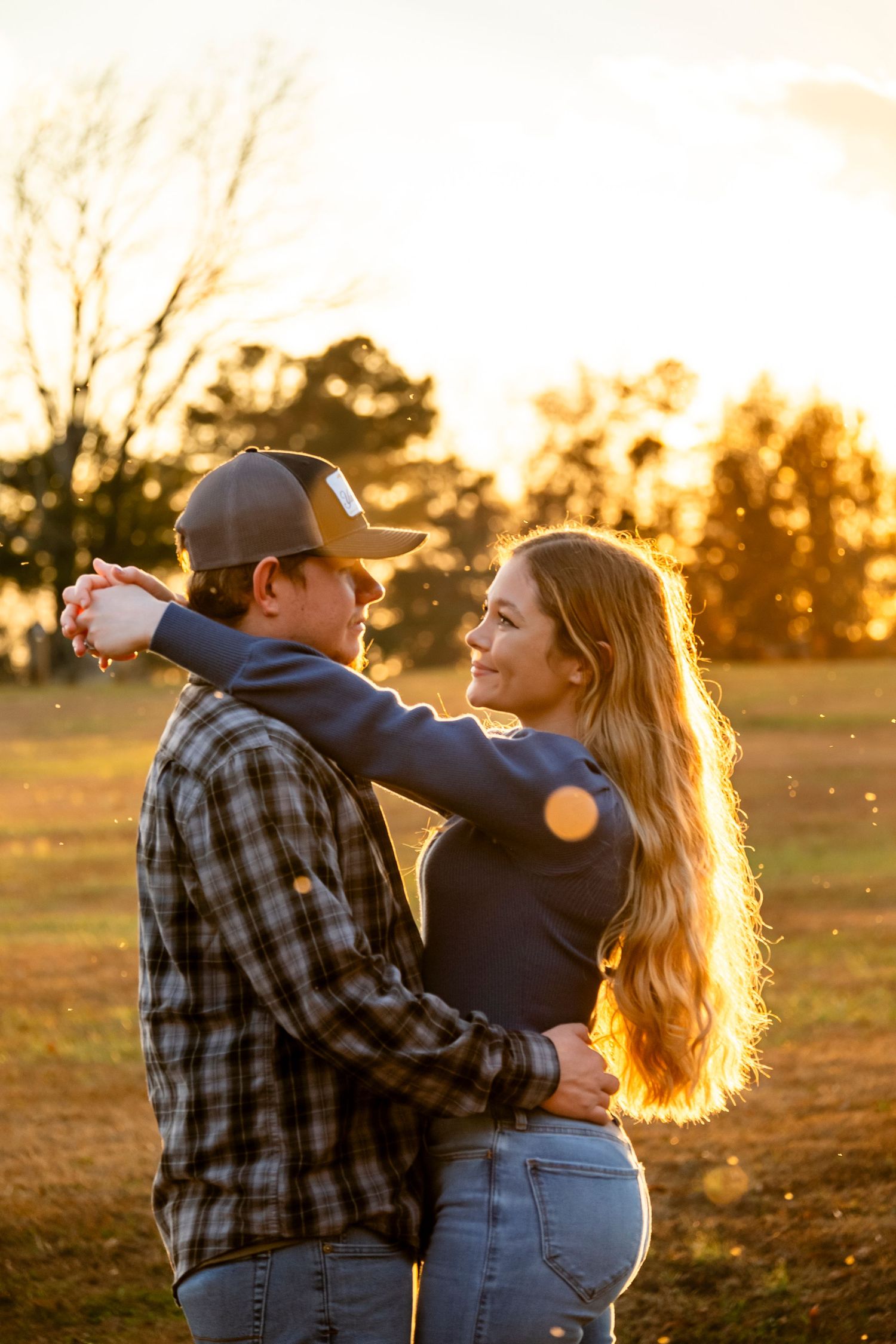 Young couple dancing together outdoors at sunset, woman laughing with golden light illuminating her long hair.