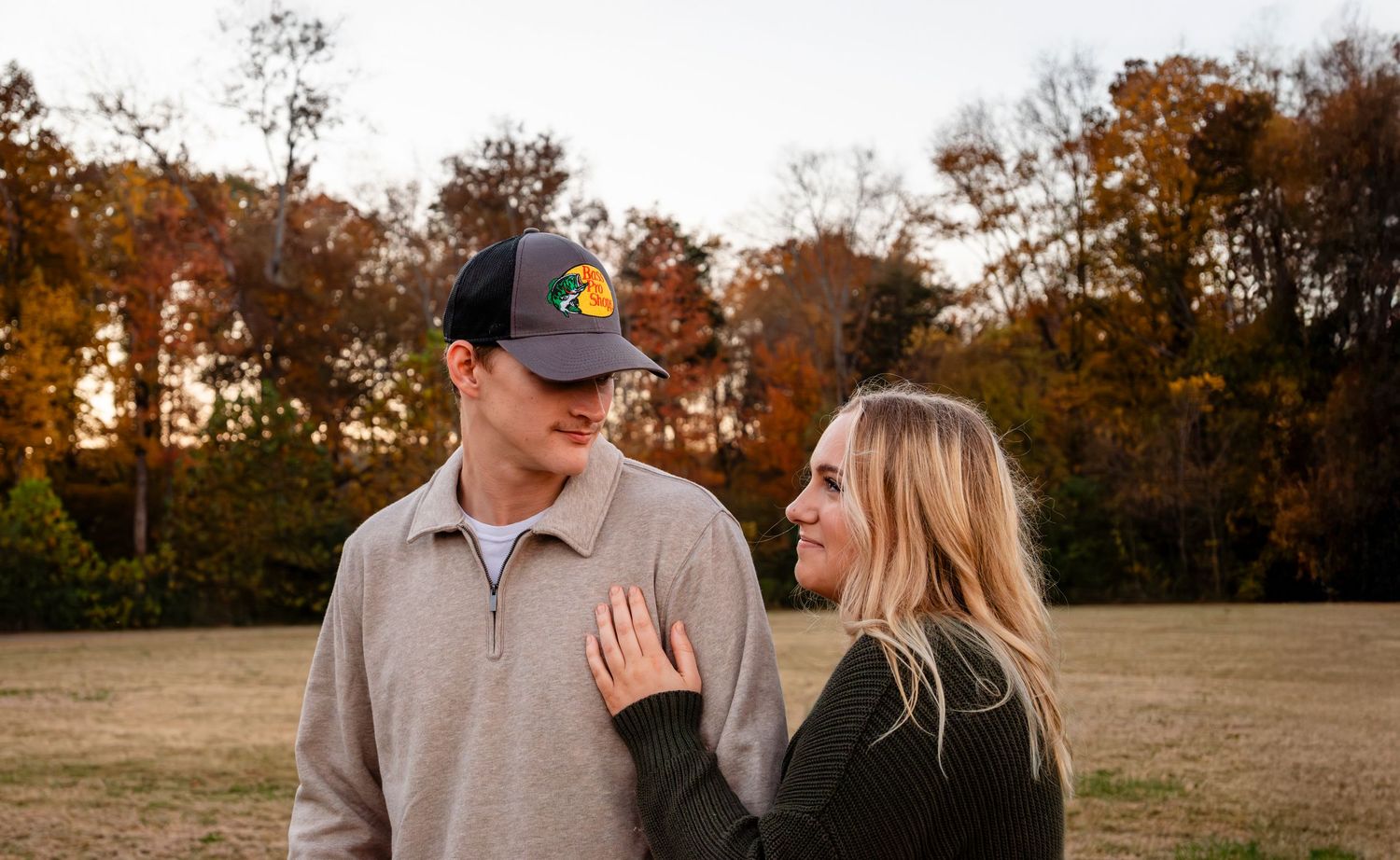 Young couple smiling at each other in an autumn field, man wearing a duck hunting cap.