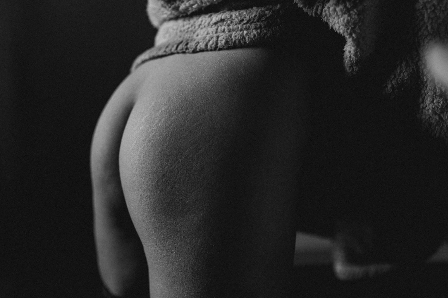 Gros plan en noir et blanc du bas du dos et des fesses nus d'une femme, révélant une peau douce au toucher.