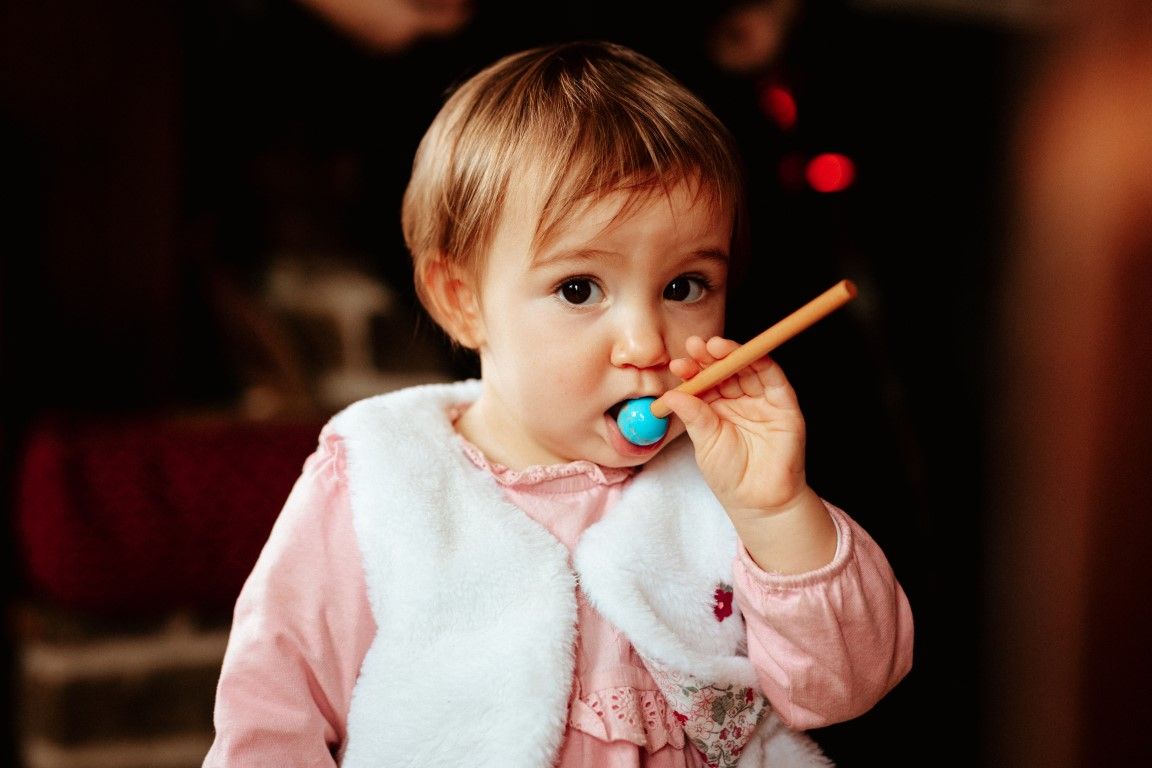 Adorable petite fille en tenue rose tenant une sucette colorée près des lumières de Noël.