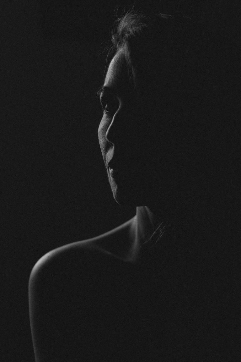 Portrait élégant en noir et blanc de profil d'une femme à l'épaule dénudée, baigné d'un éclairage en clair-obscur dramatique.