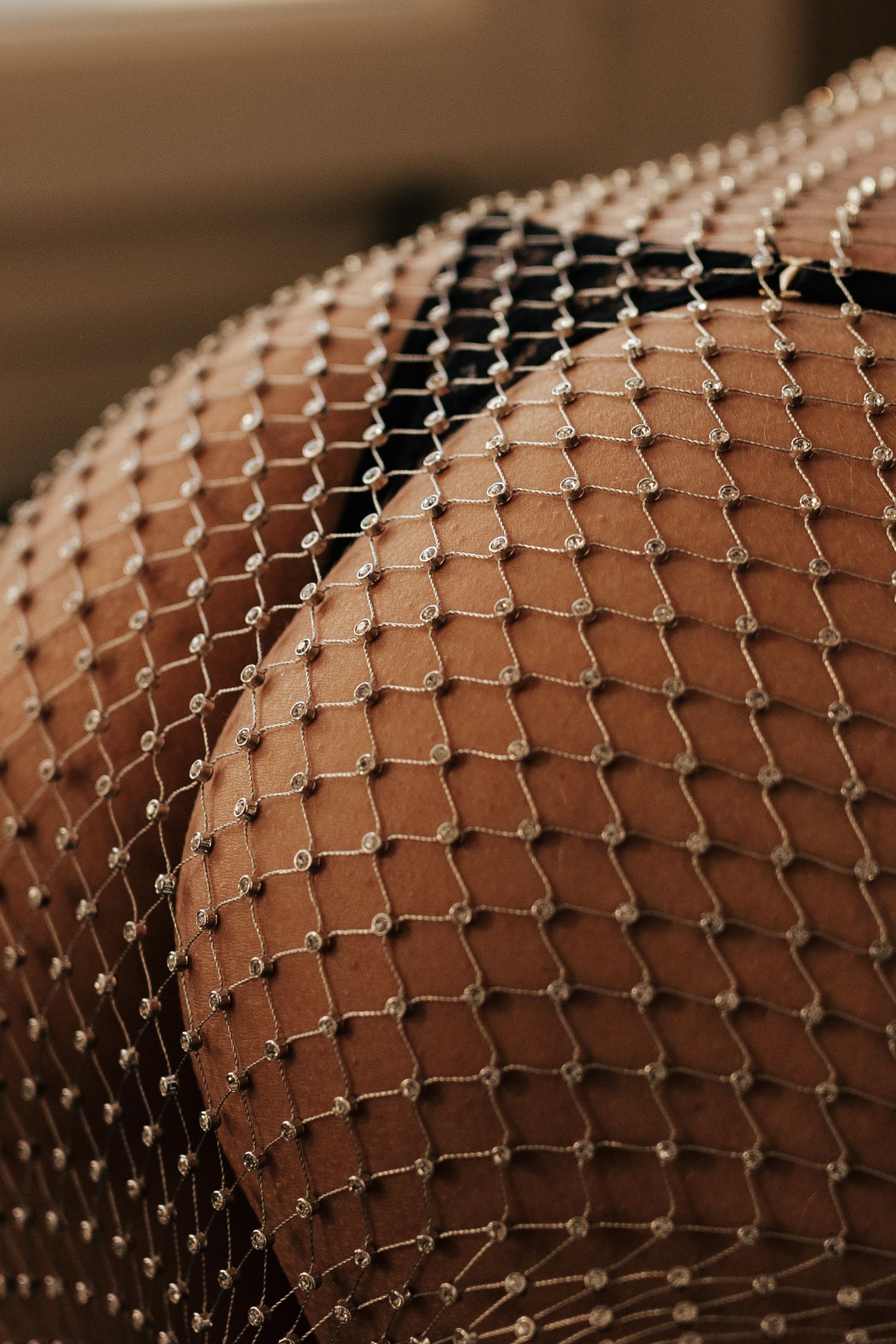 Close-up of fishnet stockings with pearl details on brown skin, showcasing elegant texture and pattern.