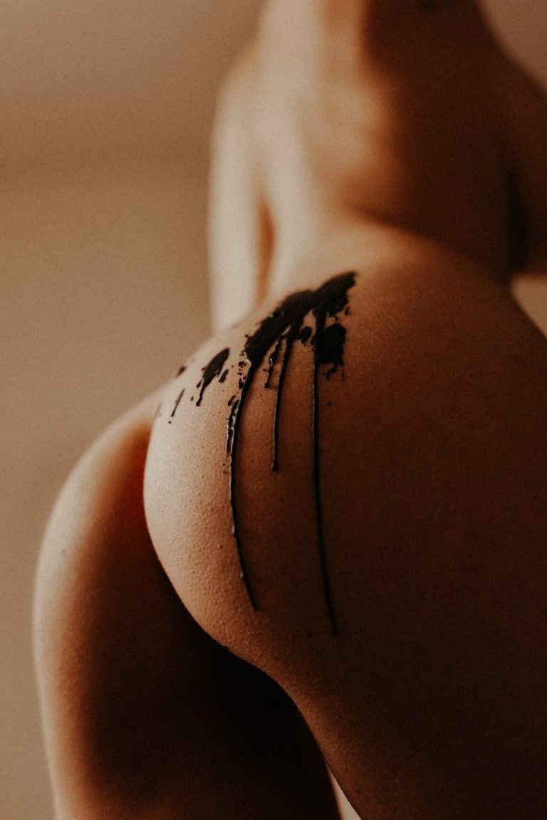 De la cire chaude noire dégouline sur le dos et les fesses nus d'une femme, dans une photographie artistique de nu.