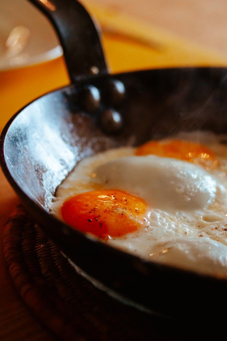 Two sunny-side up eggs frying in a black cast iron skillet with steam rising.