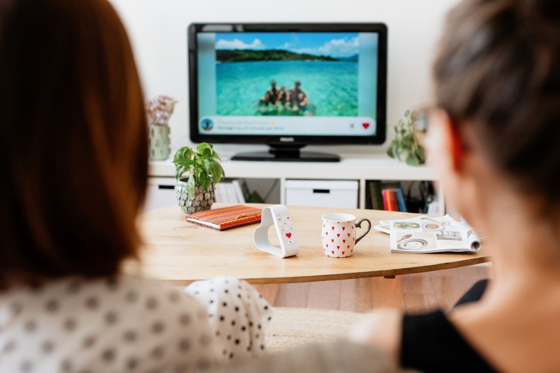 Two people watching a tropical beach photo on a TV screen in a cozy living room.