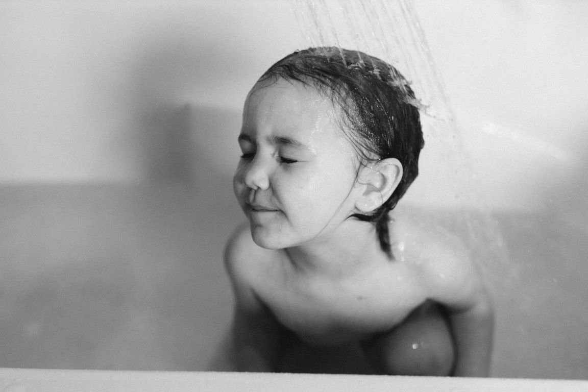 Photo en noir et blanc d'un jeune enfant prenant une douche dans une baignoire, les yeux fermés lors d'une séance photo famille