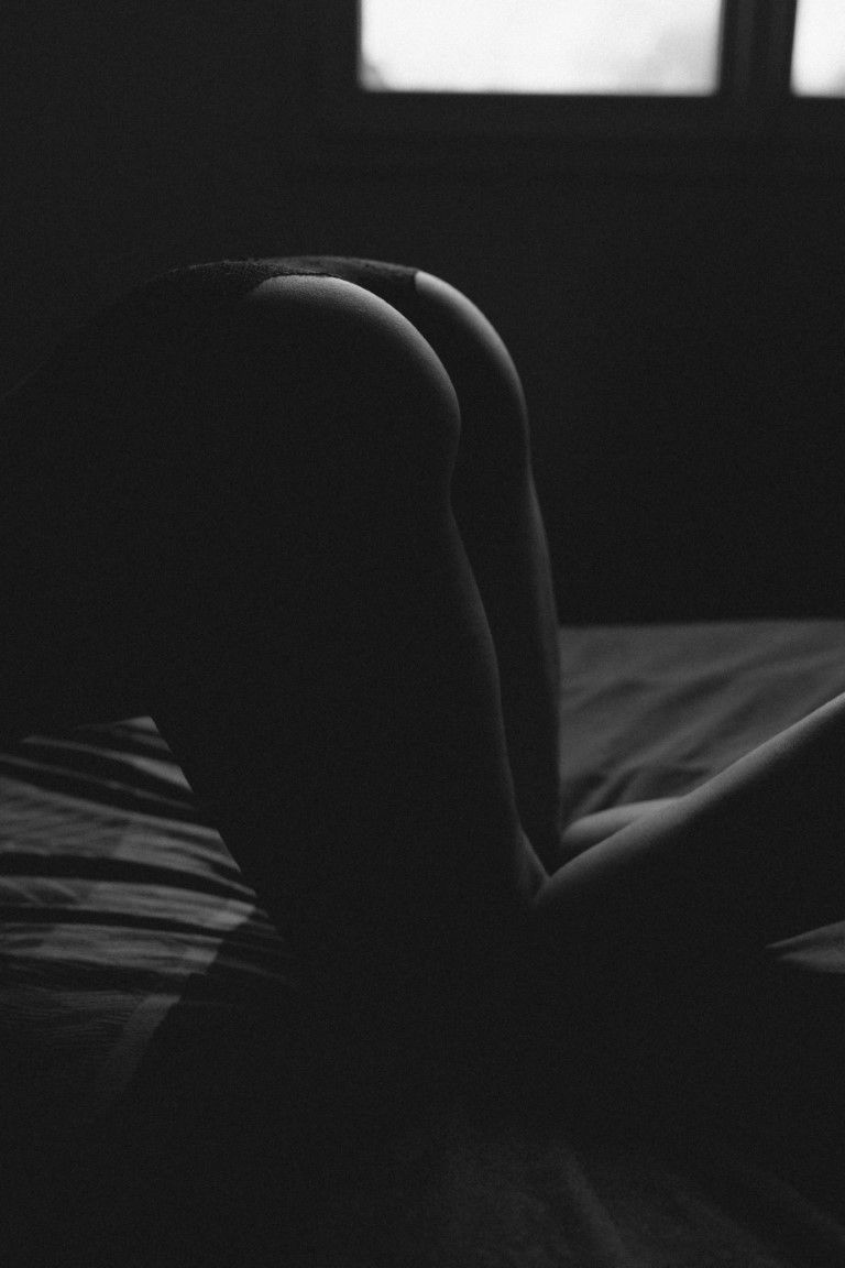 Photo artistique en noir et blanc, silhouette de boudoir mettant en valeur les courbes féminines sur un lit.