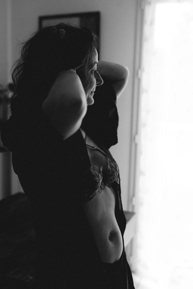 Silhouette en noir et blanc d'une femme en lingerie posant près d'une fenêtre lumineuse.