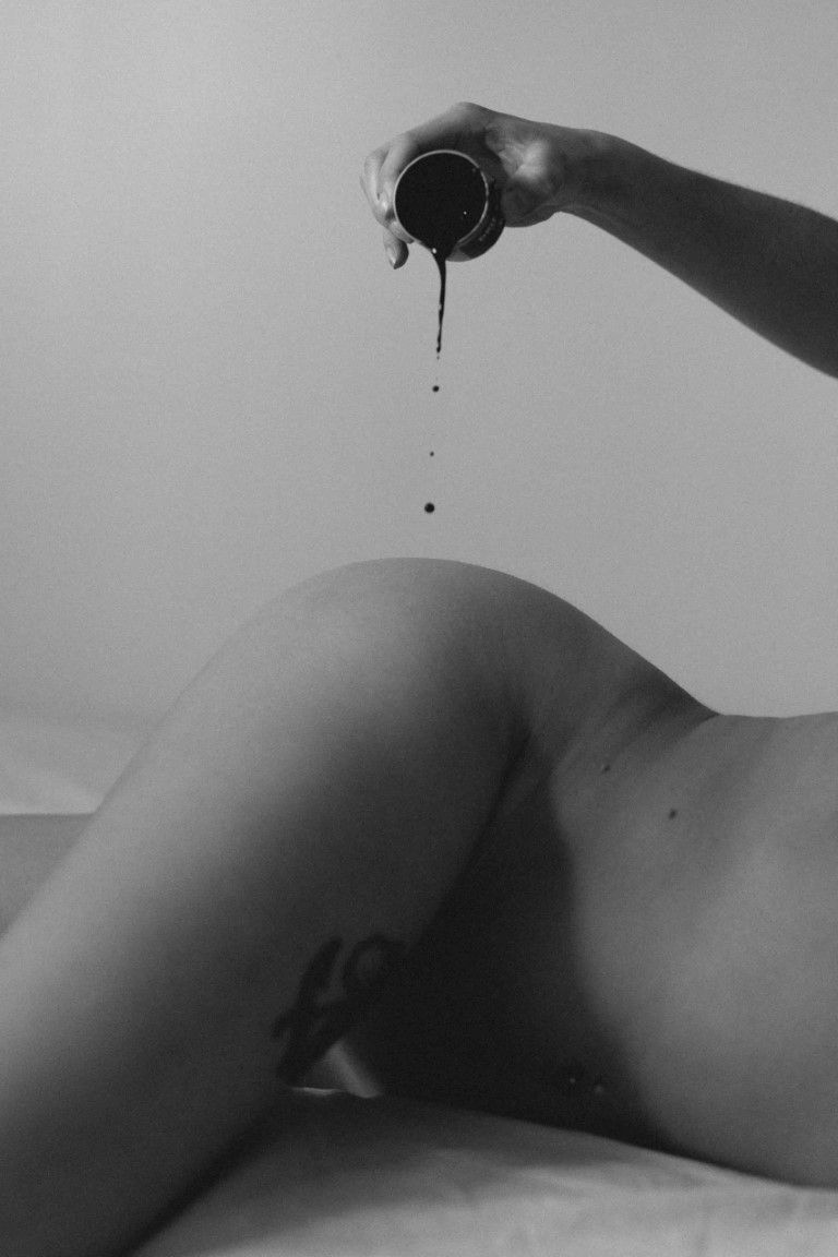 Black and white artistic photo of liquid dripping from a small cup onto a nude body.