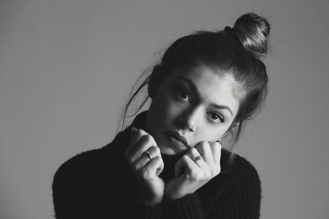 Portrait en gros plan, en noir et blanc, d'une jeune femme aux cheveux relevés en chignon et portant un pull noir.
