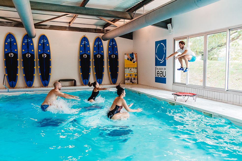 Group of people playing water polo in an indoor swimming pool with surfboards on the wall.
