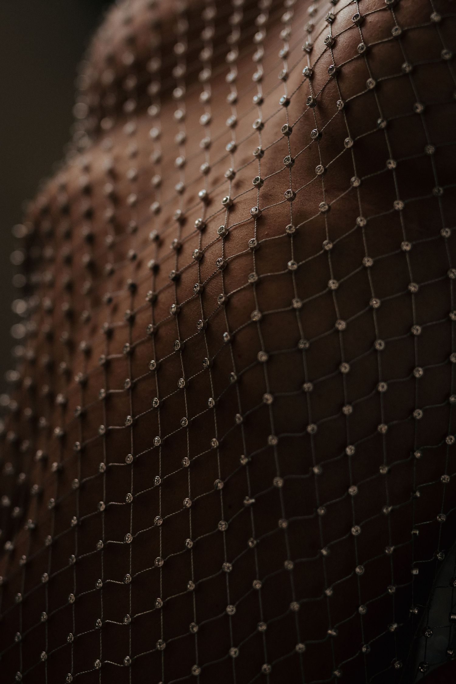 Close-up of jeweled fishnet stockings on dark skin in moody lighting, showcasing sparkling rhinestone embellishments.