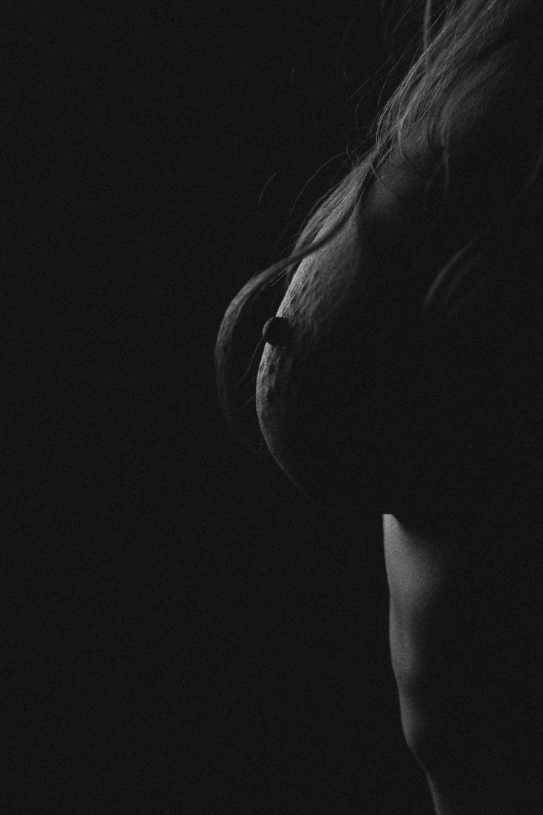 Photo artistique saisissante en noir et blanc d'un buste féminin nu, capturée dans une lumière tamisée et mystérieuse.