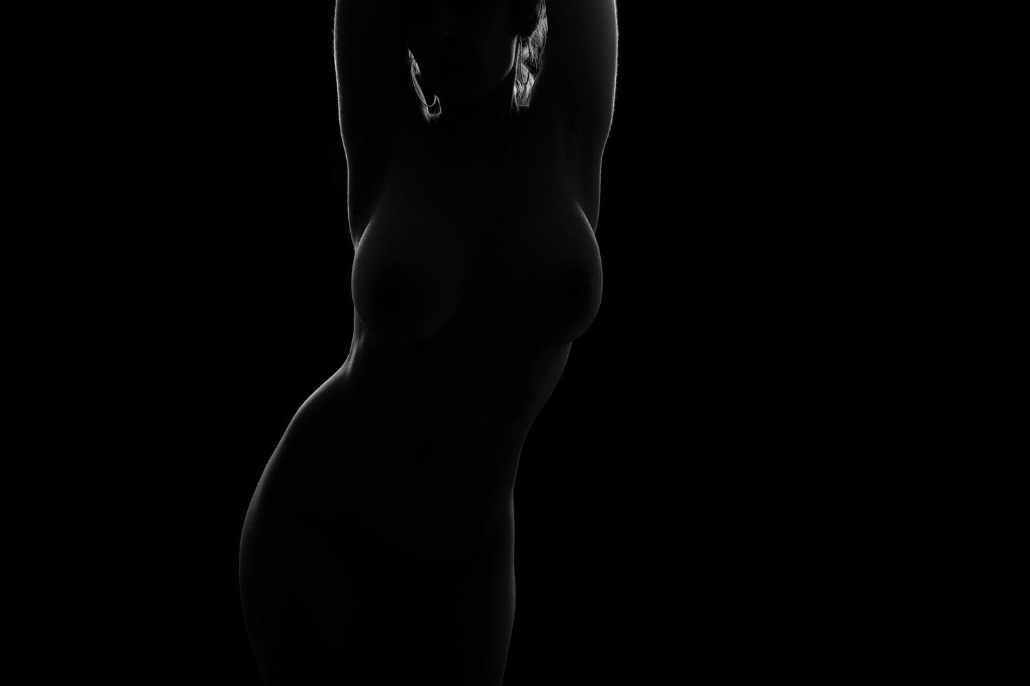 Artistic black and white silhouette photography of a female figure against a dark background.