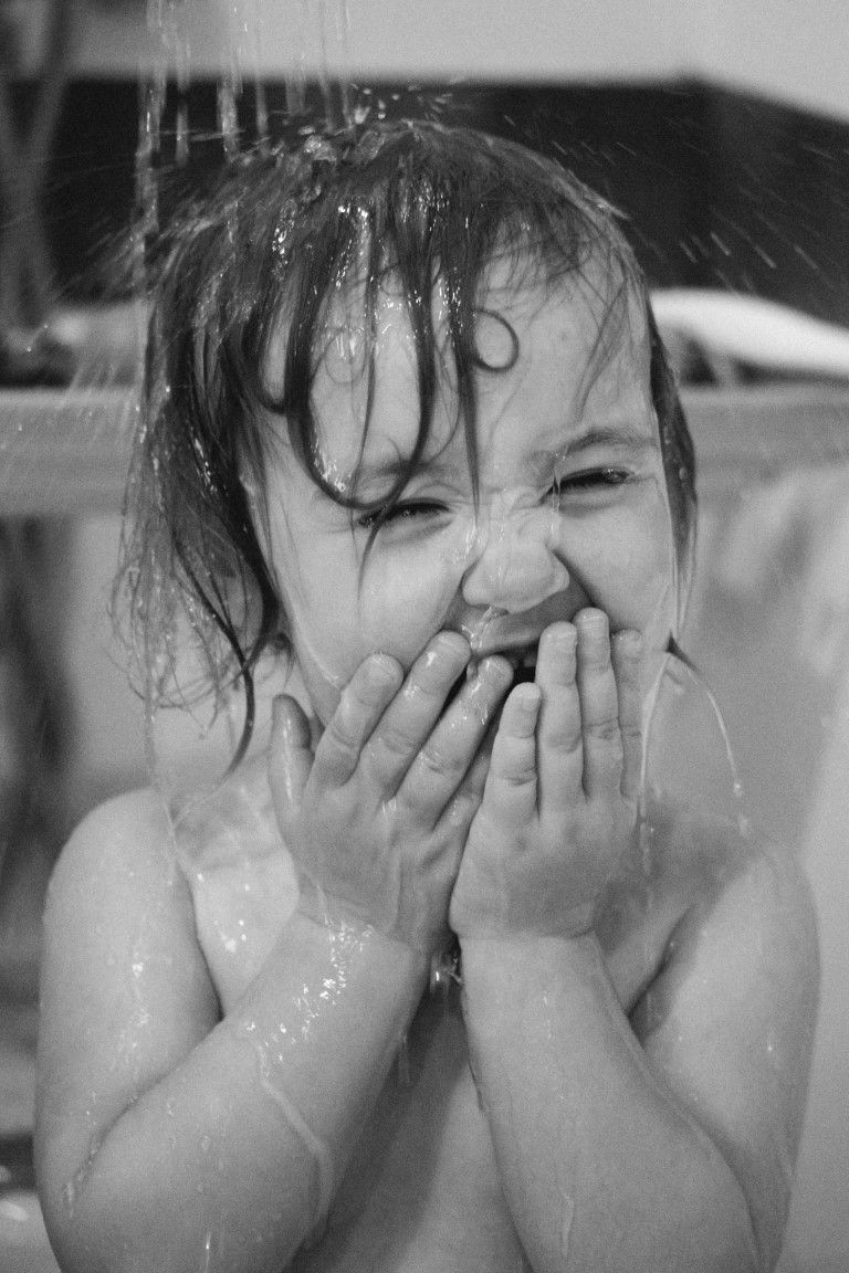 Portrait en noir et blanc d'un tout-petit riant, les cheveux mouillés et les mains sur la bouche, sous la douche.