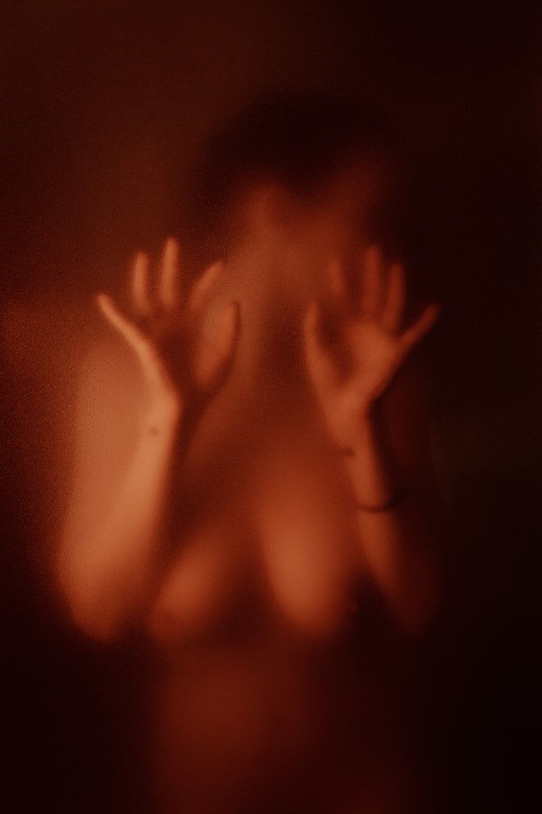 Silhouette éthérée d'une silhouette nue pressant ses mains contre une surface givrée baignée d'une chaude lumière rouge-orangée.