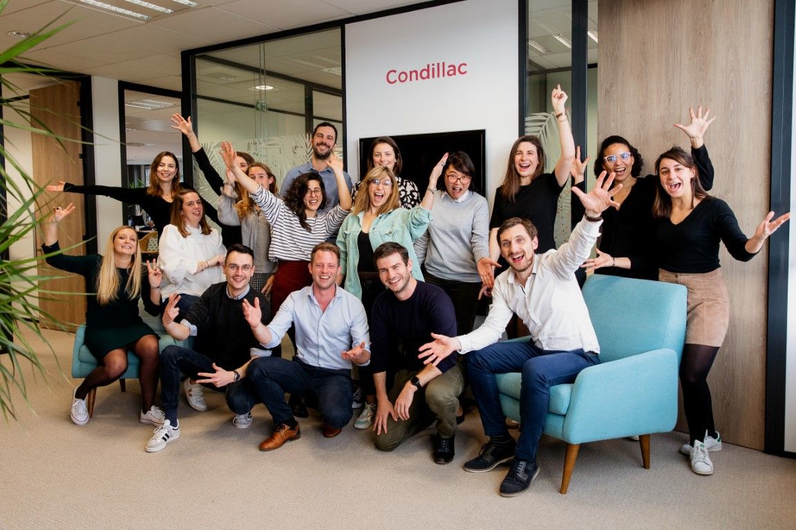 Cheerful Condillac team posing together in a bright modern office, celebrating with raised arms.