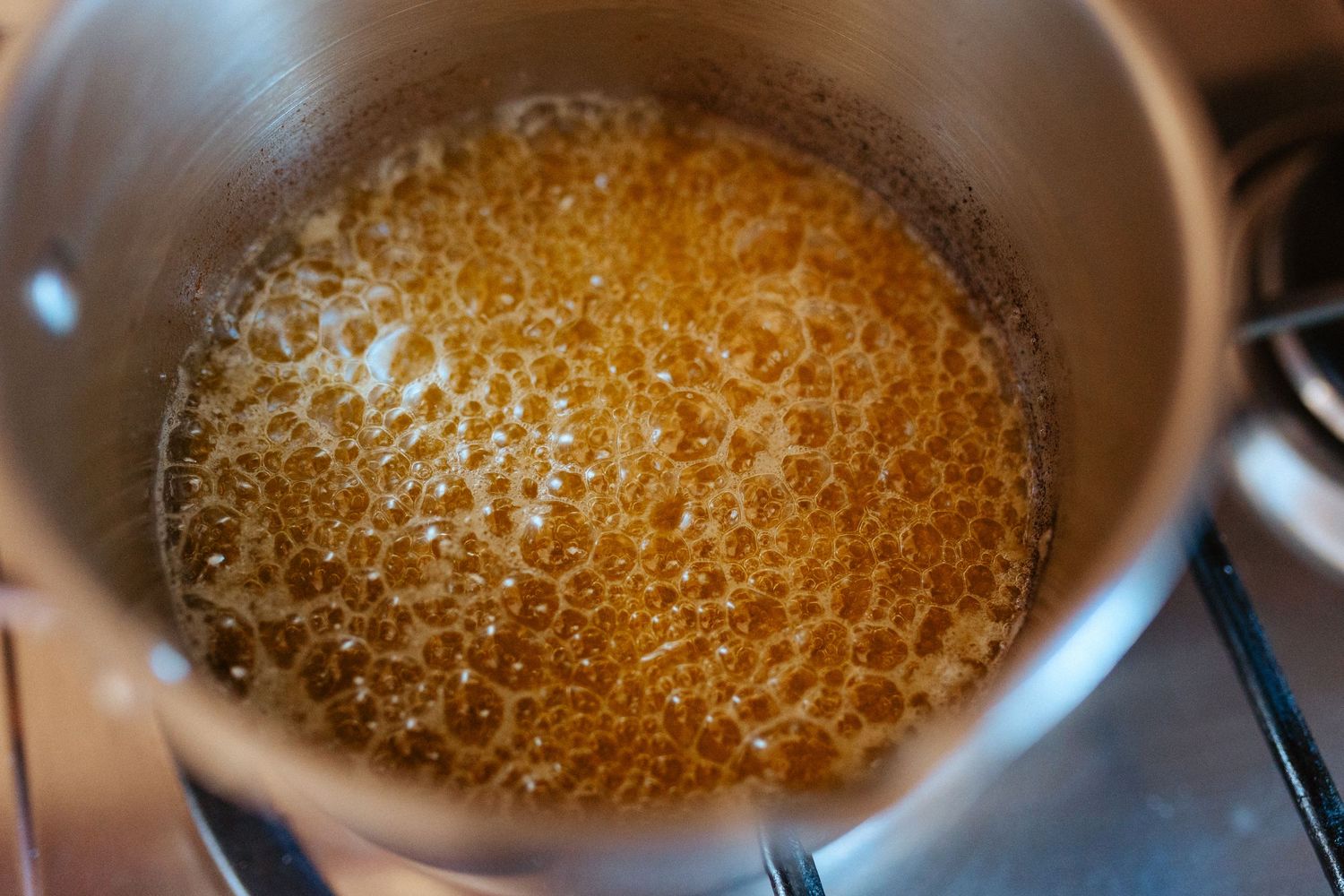 Bubbling golden caramel sauce cooking in a stainless steel saucepan on a stove.