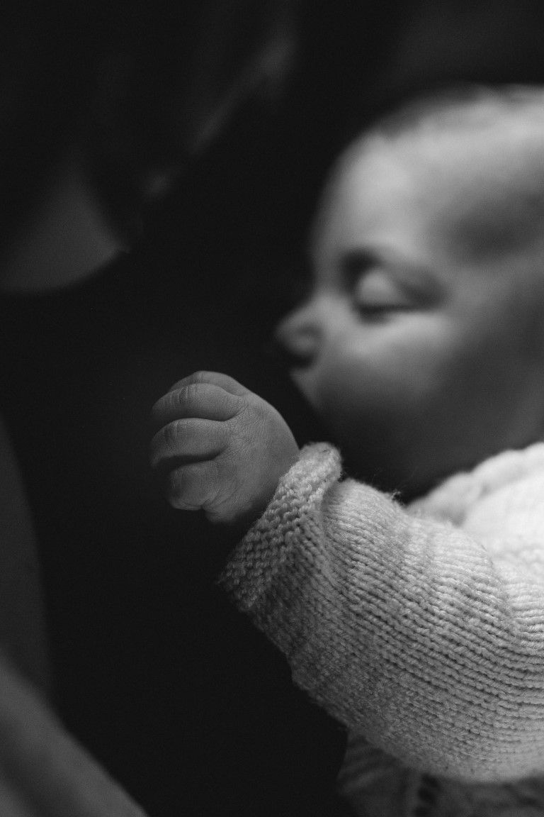 Photo en noir et blanc d'un bébé endormi, vêtu d'un pull en tricot, le petit poing serré levé.