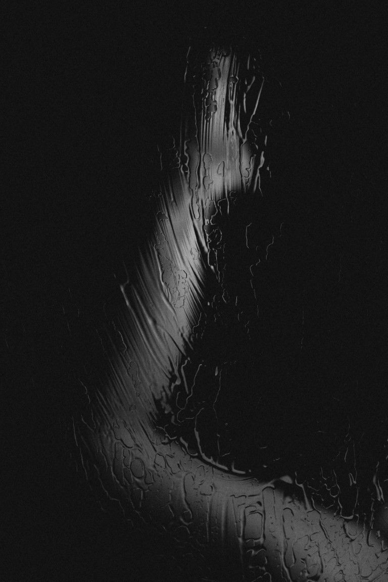 Abstract black and white photo of raindrops on glass with dramatic light and shadow contrast.