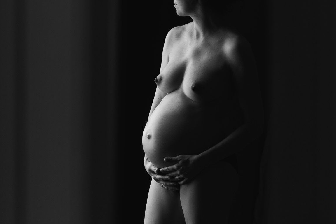 Silhouette artistique en noir et blanc d'une femme enceinte nue, berçant son ventre.