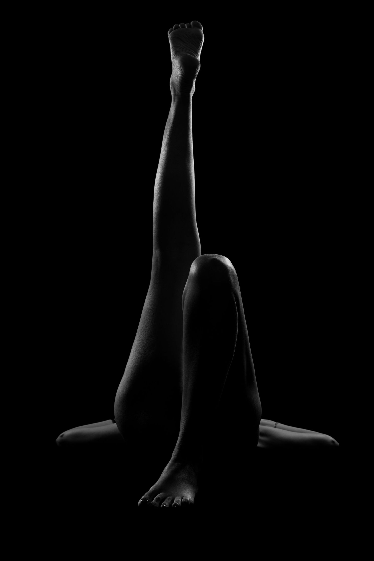 Black and white artistic photo of a persons legs posed gracefully against a dark background.