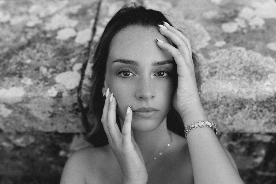 Portrait en gros plan, en noir et blanc, d'une jeune femme dont les mains encadrent le visage et qui porte un bracelet délicat.