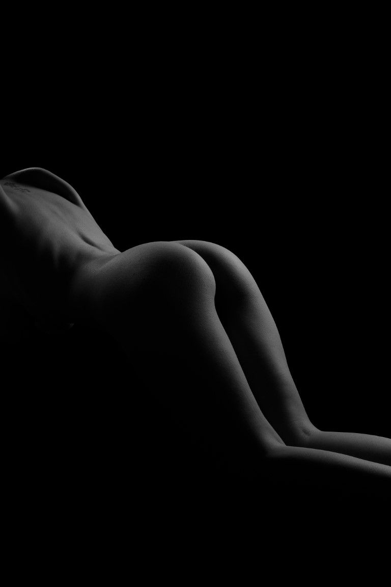 Silhouette artistique en noir et blanc d'un nu féminin, le dos et les courbes d'une femme dans une lumière tamisée.
