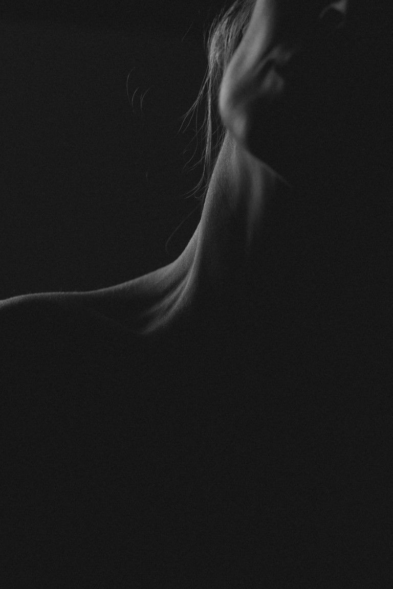 Portrait saisissant en noir et blanc capturant le cou et la mâchoire d'une femme dans une lumière douce et tamisée.