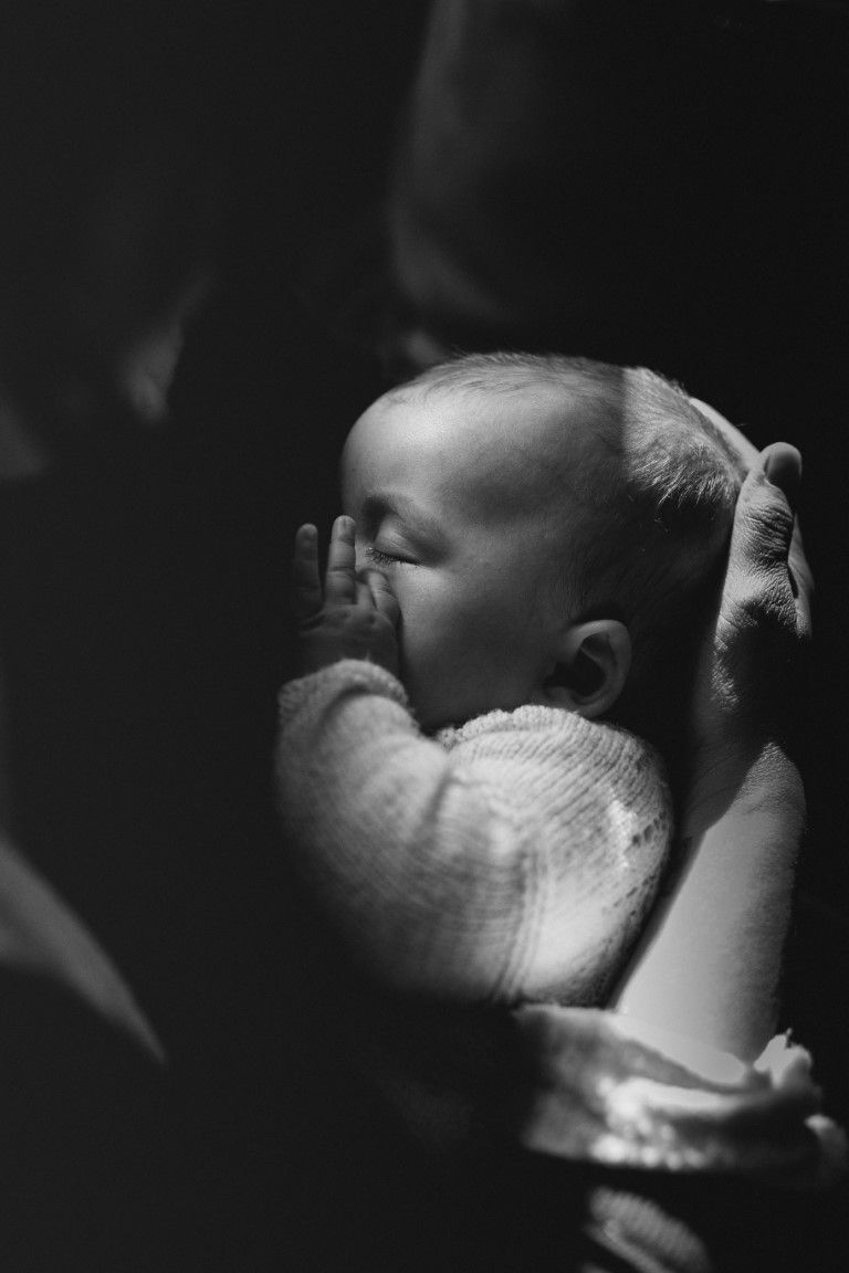 Photo artistique en noir et blanc d'un nouveau-né, les mains près du visage, blotti dans les bras.