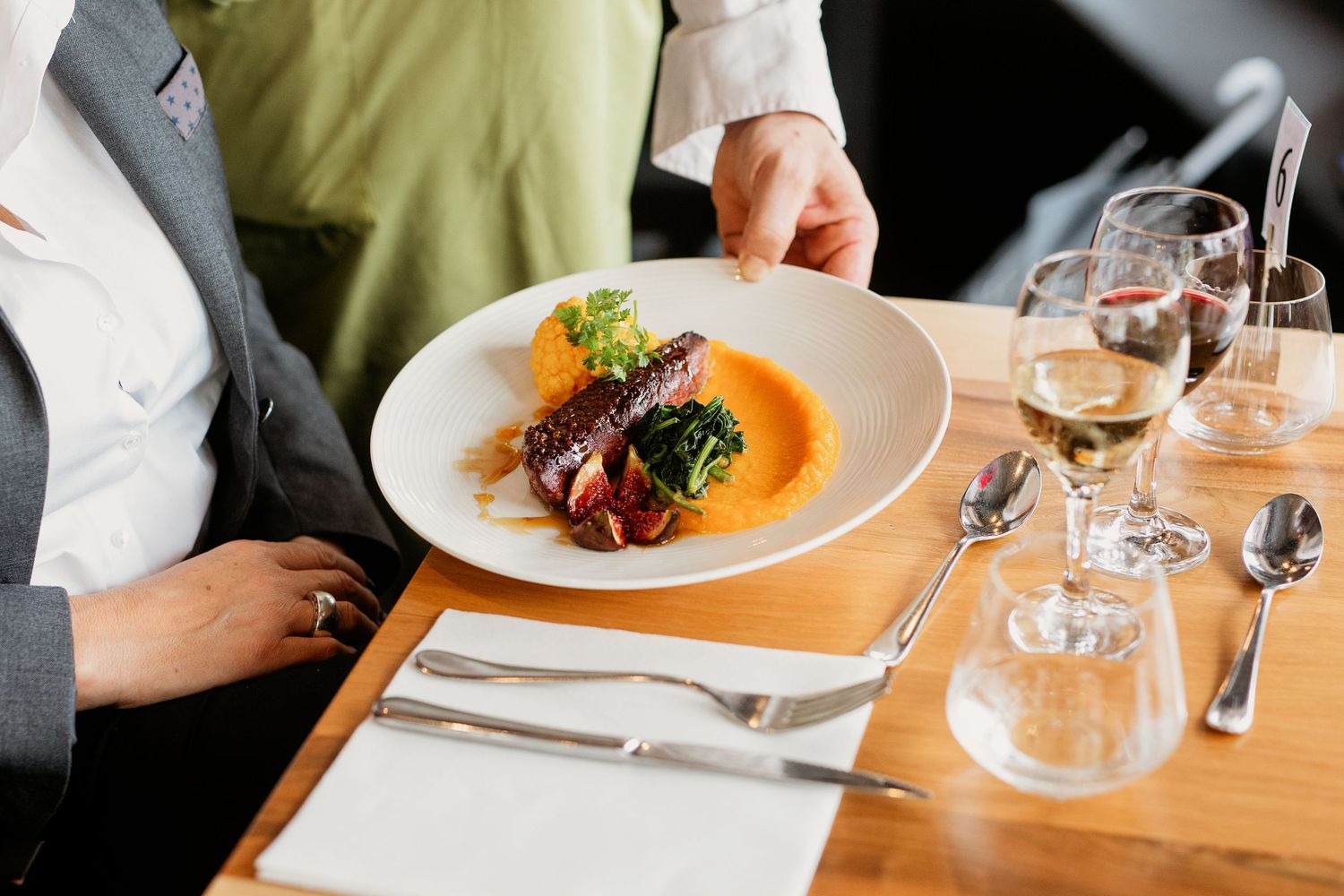 Waiter serving an elegant gourmet dish with meat and vegetables on a white plate at a fine dining restaurant.