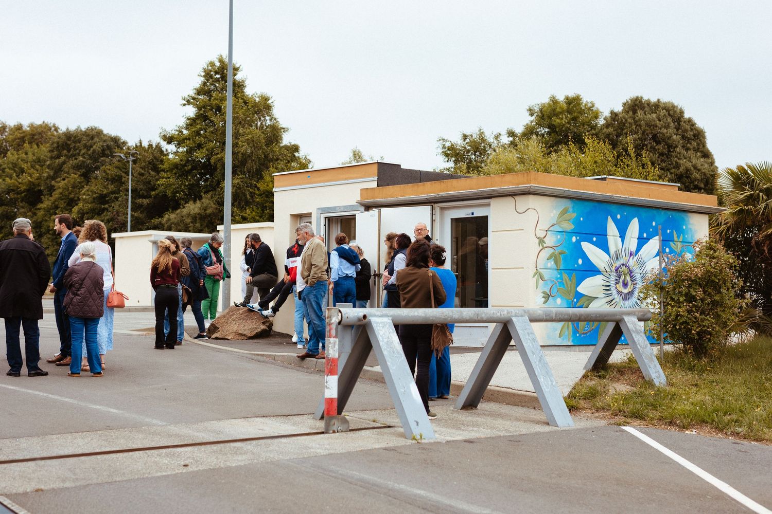 People queuing outside a small decorated building with colorful mural artwork at an outdoor event on a cloudy day.