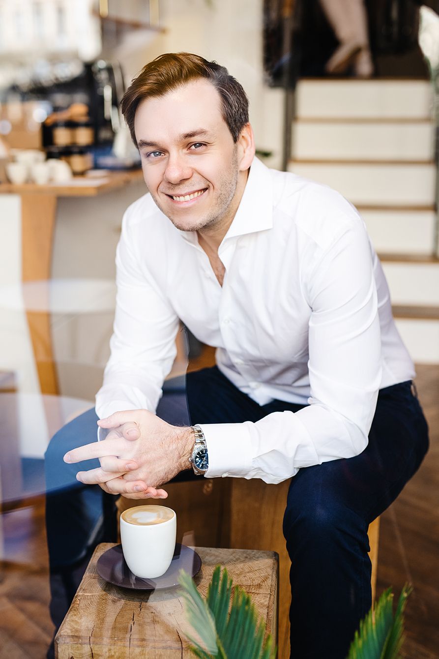 Smiling man in white shirt sitting in cafe with coffee cup on wooden table.