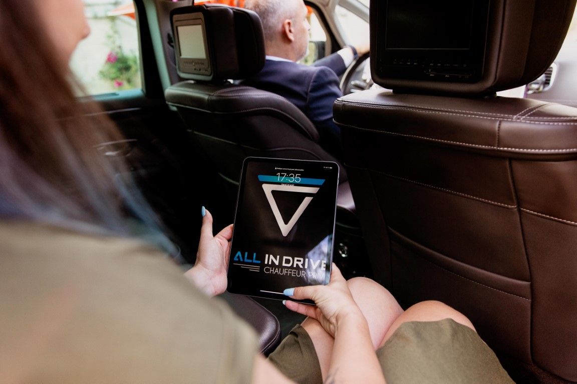 Female passenger viewing All In Drive app on tablet in luxury car backseat.