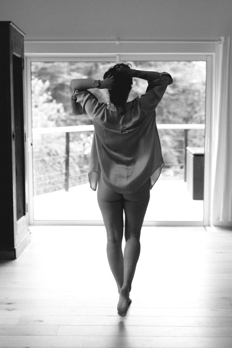 Black and white rear view of a woman in a sheer shirt walking toward a glass door.