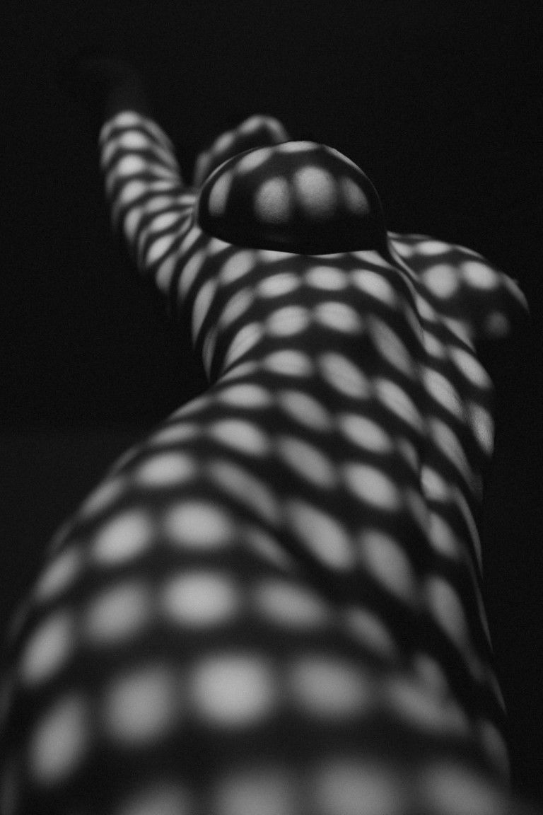 Black and white abstract photo of a human body with geometric dot light patterns creating a striking visual texture.
