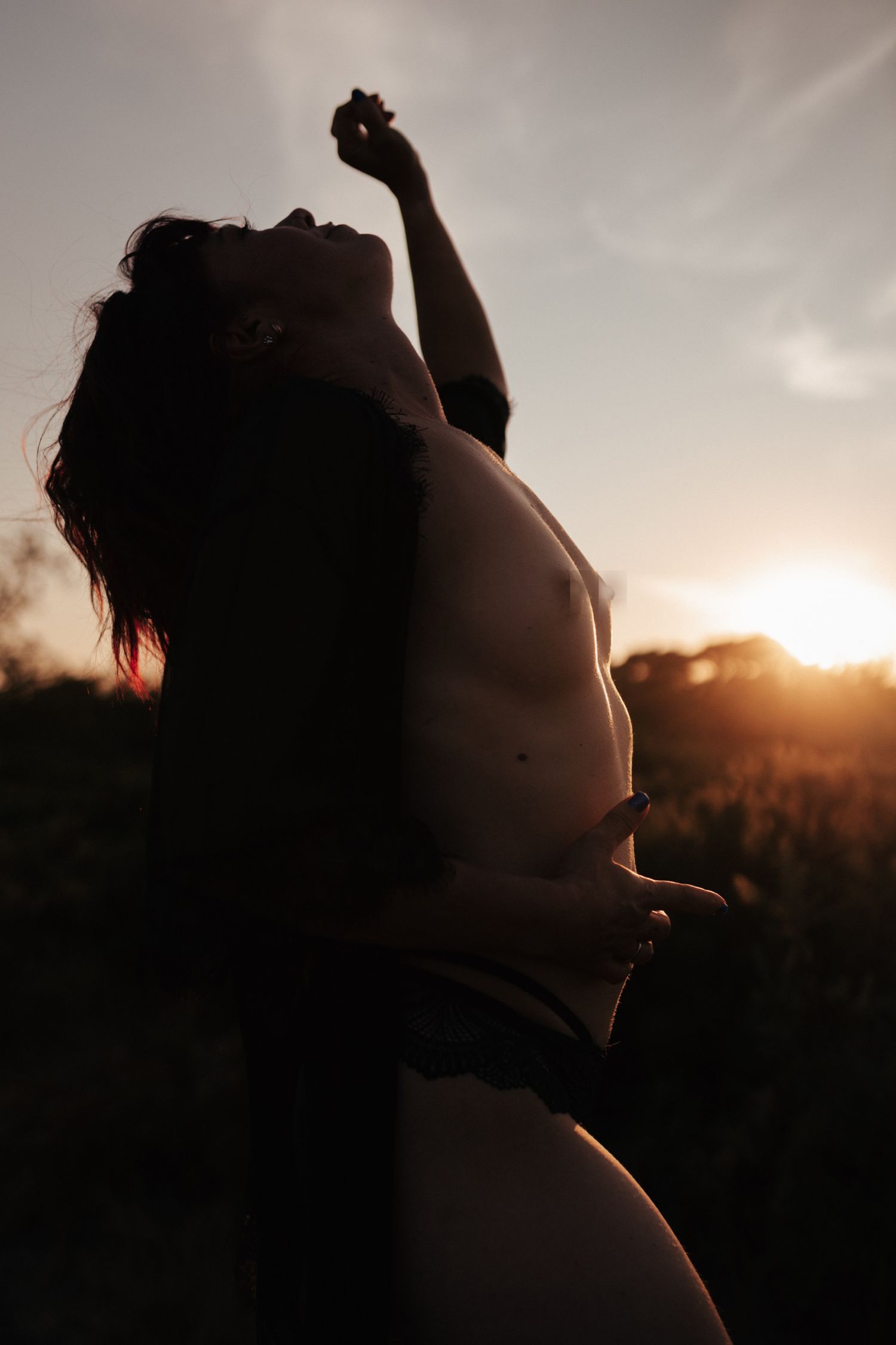 Silhouette of a person posing against a golden sunset sky, arms raised, backlit by warm glowing light.