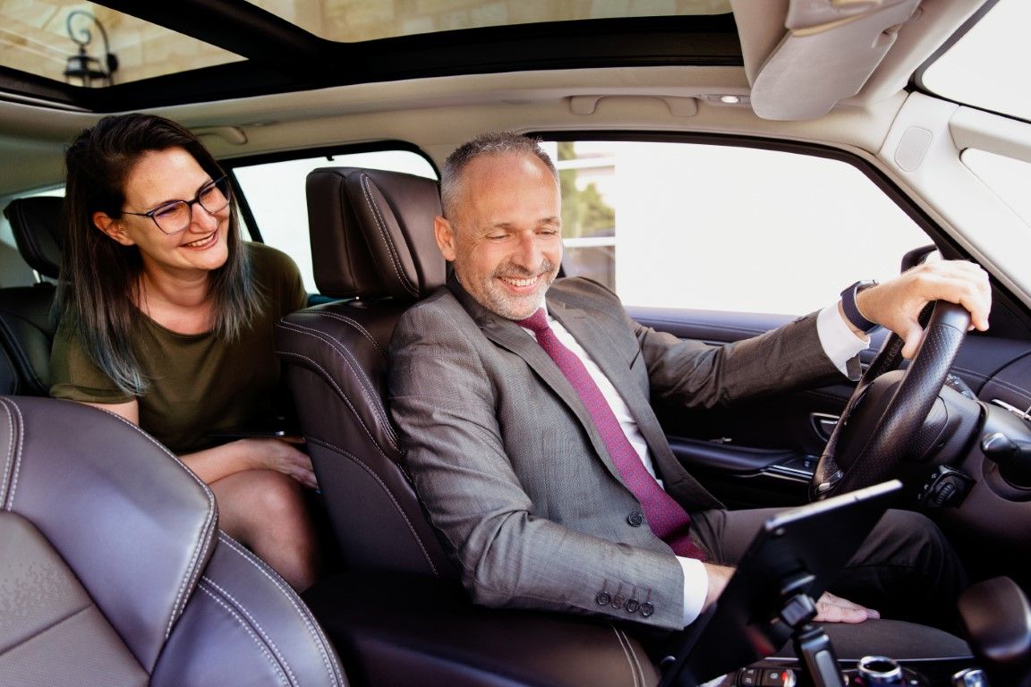 Smiling woman and male chauffeur sitting inside luxury black car with leather seats.