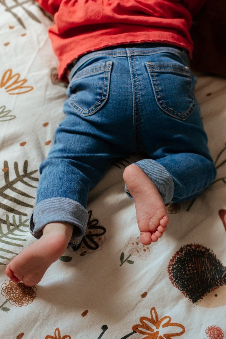 Bébé portant un jean en denim retroussé, allongé face contre terre sur une couverture à fleurs.