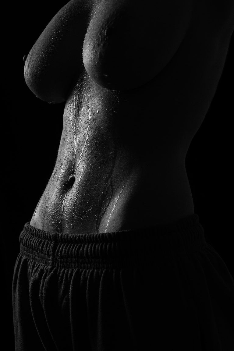 Torse féminin mouillé en noir et blanc avec des gouttelettes d'eau, portant un short foncé.