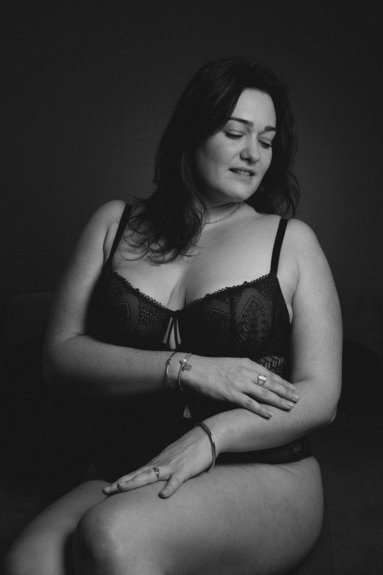 Black and white portrait of a woman in black lace lingerie sitting gracefully.