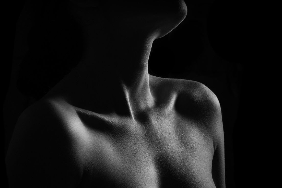 Black and white artistic photo of bare shoulders and collarbone in dramatic lighting.