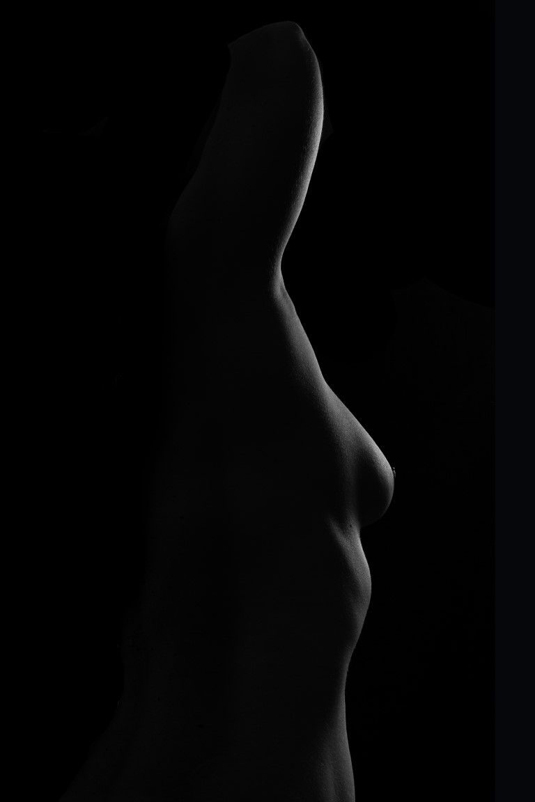 Portrait artistique en noir et blanc d'une femme regardant par-dessus son épaule, baignée d'un éclairage tamisé et dramatique.