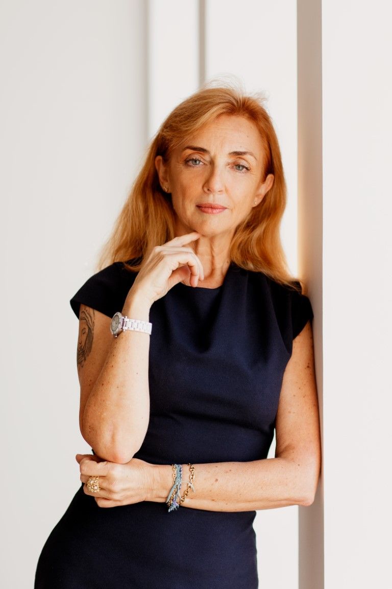 Sophisticated woman with red hair in navy dress posing thoughtfully against white wall.